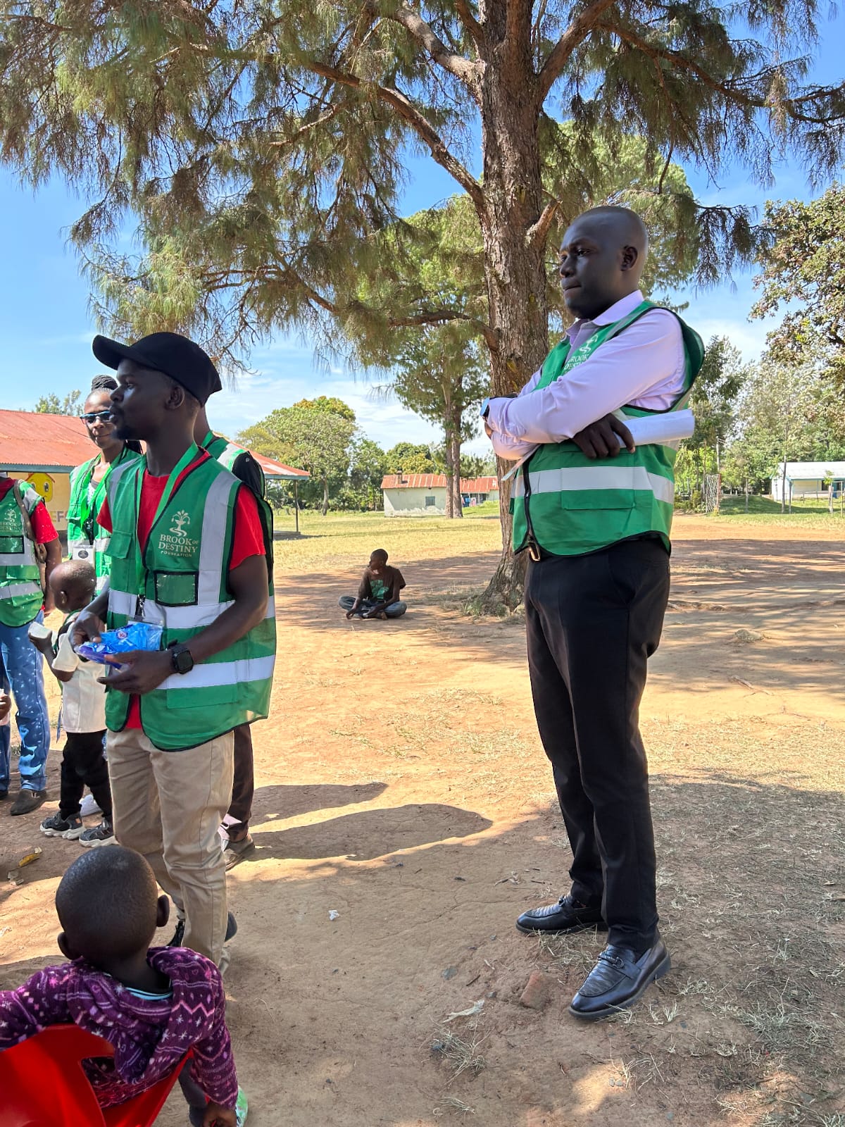 Volunteers in reflective jackets speaking with residents in a village compound